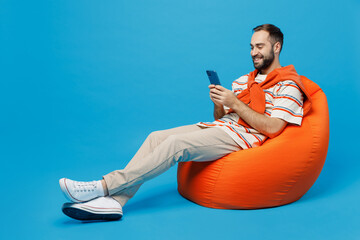 Full body young smiling satisfied fun happy man 20s wear orange striped t-shirt sit in bag chair...