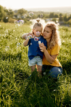 Little caucasian girl and mom playing with bubbles