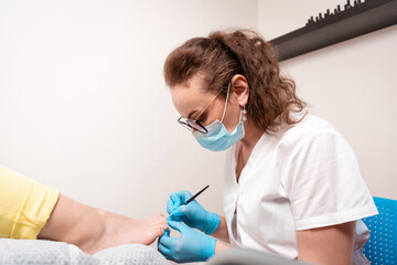 Woman podiatrist in blue gloves does a caring procedure for the client's nails. The concept of...