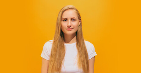 Emotional young girl with long blond hair wearing white t-shirt posing isolated on yellow background. Concept of emotions, facial expression, youth, fashion