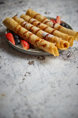 Plate of delicious crepes roll with fresh fruits and chocolate