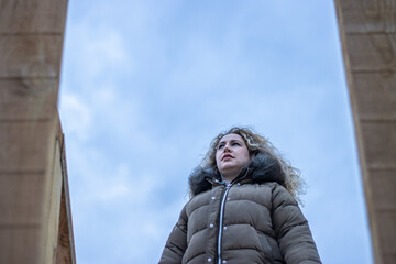 A woman in profile on an autumn day wearing a coat and with her eyes closed as the wind blows in her face in the open air.