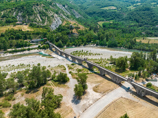 Aerial view. Drought and dry rivers. Roman bridge of Bobbio over the Trebbia river, Piacenza, Emilia-Romagna. Italy. River bed with stones and vegetation. Called hunchback bridge