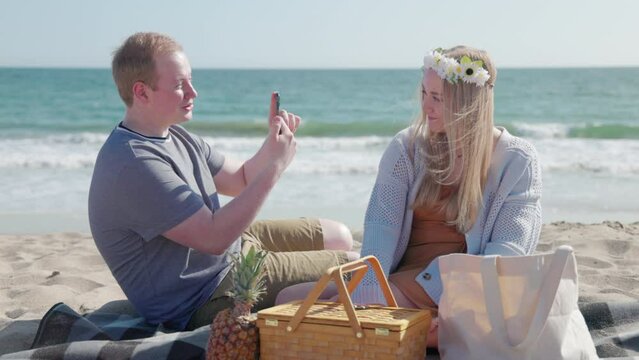 Laughing young family on a romantic date at the coastal area. Man taking photo of his girlfriend in a beautiful flower crown. High quality 4k footage
