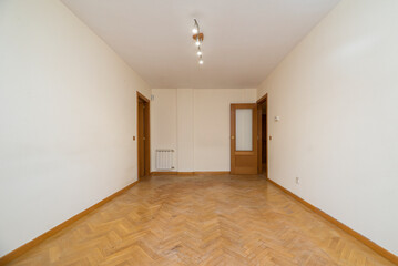 Empty room with white painted walls, herringbone oak parquet flooring, matching woodwork and white radiator