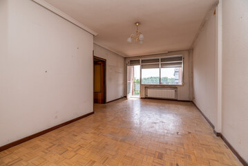 Empty room with white painted walls, oak parquet floor, white aluminum radiator under the large aluminum window of a terrace