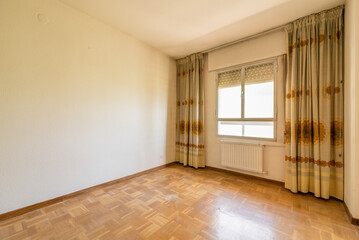 Empty room with white painted walls, aluminum window with radiator below and kitsch vintage curtains