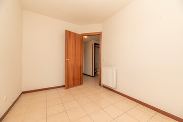 Empty room with white painted walls, cream ceramic floor, reddish wood carpentry and white radiator