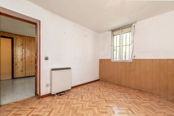 Empty living room with white and PVC painted walls and tongue and groove pine wood, oak parquet flooring and white ceramic stoneware