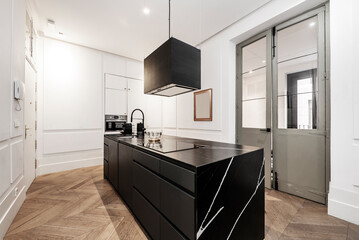 Modern kitchen with central island of wood and black marble, matching extractor hood and oak wood floor