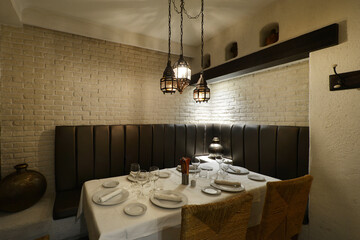 Dining room restaurant with rectangular wooden table with white tablecloth, food service station and natural fiber chairs