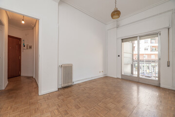 Empty living room with metal radiator, oak parquet floors and sliding to a terrace with aluminum and glass sliding doors