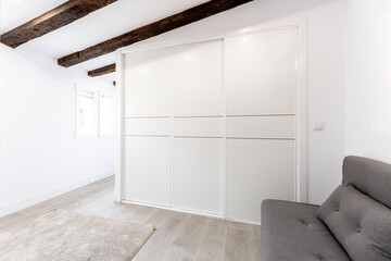 Fototapeta premium Wardrobe with three white sliding doors in a room with sloping ceilings and ceiling beams