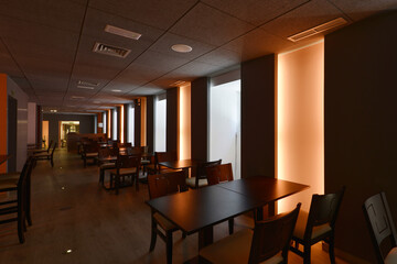 Dining room of a restaurant with wooden tables matching the chairs and neon lights on the walls in a dark room