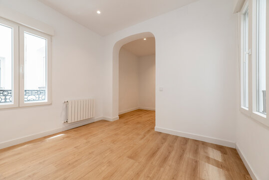 Empty room with white painted walls, oak laminate flooring, white aluminum windows and basket weave between rooms