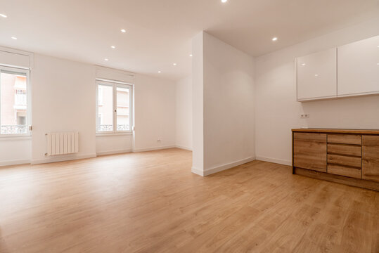 Empty living room with open kitchen with chestnut wood furniture, wooden floors and plain white painted walls