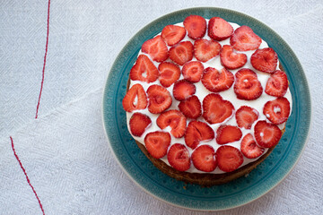 Cake with strawberries and cream on blue plate. Summer Strawberry and Cream sponge Layer Cake on white table cloth background. Top view, copy space. Midsummer food dessert