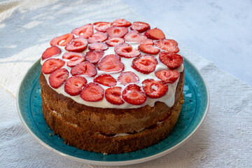 Cake with strawberries and cream on blue plate. Summer Strawberry and Cream sponge Layer Cake on white table cloth background. Top view, copy space. Midsummer food dessert