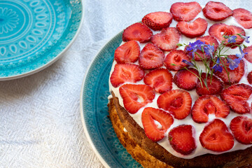 Cake with strawberries and cream on blue plate. Summer Strawberry and Cream sponge Layer Cake on white table cloth background. Top view, copy space. Midsummer food dessert
