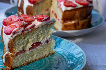 Piece of cake with strawberries and whipped cream on blue plate. Summer Strawberry and Cream sponge Layer Cake on white table cloth background. Top view, copy space. Midsummer food dessert
