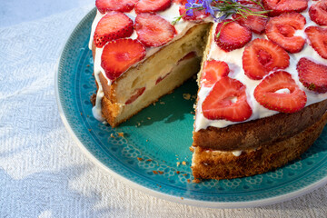 Cake with strawberries and cream on blue plate. Summer Strawberry and Cream sponge Layer Cake on white table cloth background. Top view, copy space. Midsummer food dessert