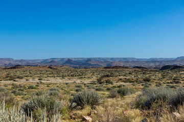 Fototapeta na wymiar Semi arid landscape of the Augrabies National Park in the Northern Cape, South Africa. Mountains and clear blu skies in the background. Grass and small shrubs in the foreground. 