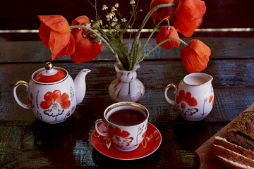 Traditional poppy seed bun with cup of tea and milk near poppies flowers and dishes with poppies ornaments. Delicious breakfast in summer. Lifestyle photography