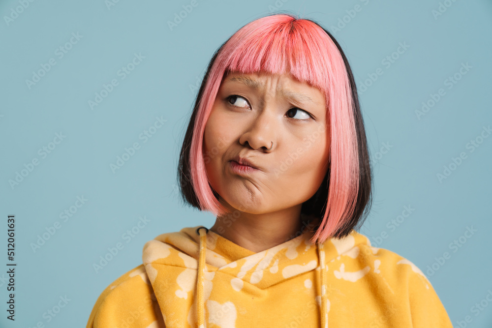 Wall mural asian girl with pink hair and piercing frowning while looking aside