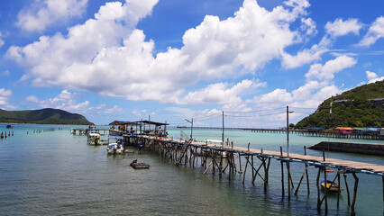 Wooden bridge pathway for group of people, tour, tourist walk to get in speedboat and longtail boat to take trip on sea go to island and fishing fish and squid with white clouds, blue sky background.