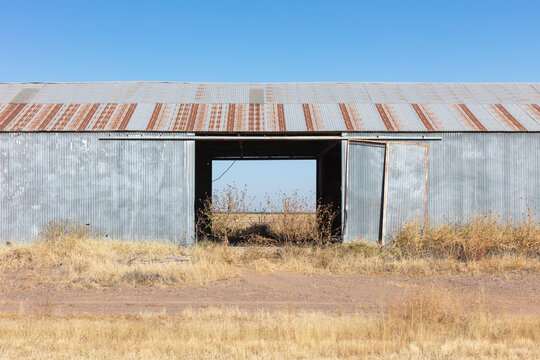 Abandoned rusting metal farm building with large open doors.
