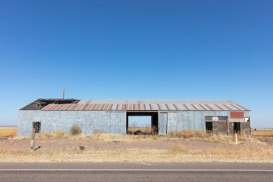 Abandoned rusting metal farm building with large open doors.