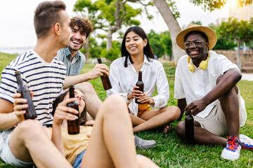 Young group of diverse best friends hanging out in city park while drinking beer - Focus on african man looking at camera