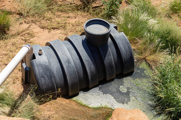 Black plastic septic tank that is partially buried in the ground. The tank is leaking dirty...