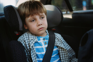 Little boy feeling sick travelling by car sitting in child seat fastened with belt