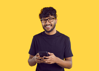 Crop shot of smiling millennial Indian guy in glasses isolated on yellow studio background using...
