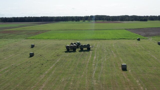 Aerial Shot of a Tractor loading two large Balls of Straw or Bales of Hay on to the carriage with stacked Bales of Hay.