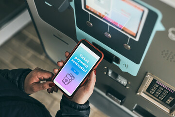 Woman buying ticket at ticket machine paying using mobile payment app on smartphone. Female buying bus public transpoort ticket in vending machine. Purchasing car parking ticket using mobile phone - obrazy, fototapety, plakaty