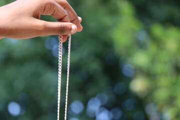 Holding a new silver chain in hand on green nature background
