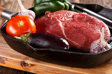 Raw piece of meat for grilling with vegetables in a cast iron pan, close-up, eating out, studio photo