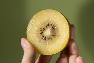 .Cut yellow kiwi in hands on a green background with shadows. Close-up.