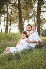 Naklejka na ściany i meble Happy pregnant couple with daughter in summer nature.
