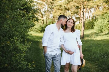 Happy and young pregnant couple hugging in nature