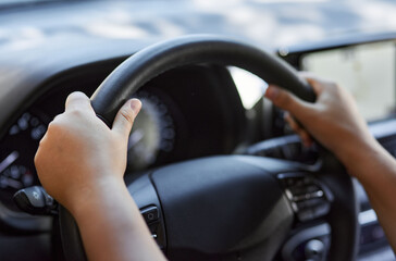 A close up shot of a young woman's hands on the steering wheel of a car..