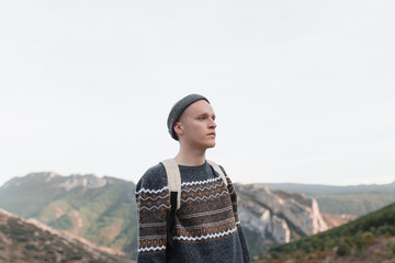 Boy with hat and backpack looks towards the mountains