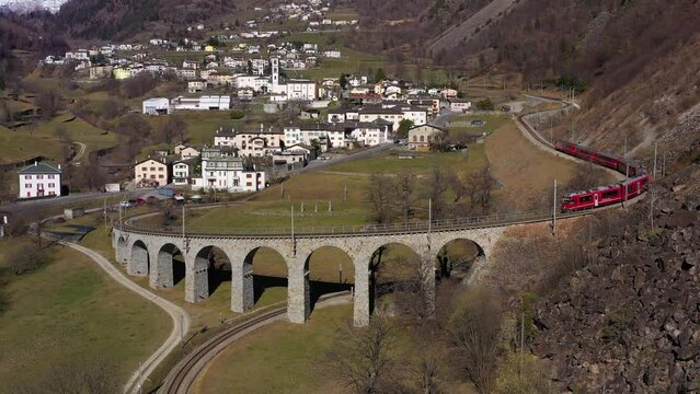 Train on Brusio Spiral Viaduct in Switzerland on Sunny Day. Bernina Railway. Swiss Alps. Aerial View. Drone Flies Backwards and Upwards