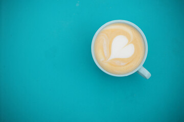 A cup of cappuccino with heart  on a aquamarine surface. View from above