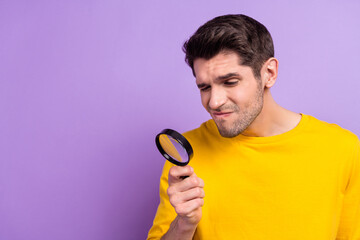 Photo of thoughtful minded funny man use magnifying loupe try to find something isolated on purple...