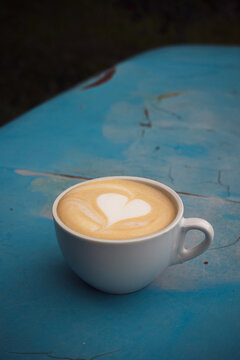 A cup of cappuccino with heart on a shabby blue surface.