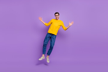 Fototapeta na wymiar Full length photo of cheerful carefree man jumping up wear yellow shirt and denim isolated on violet color background