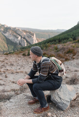 Boy with hat and backpack sitting on a rock in the middle of mountains